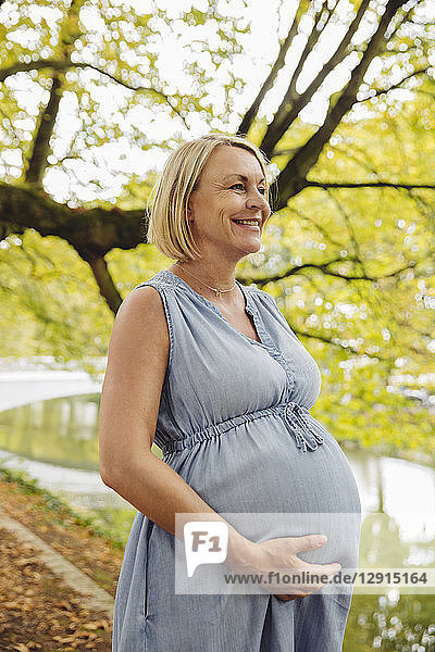 Happy mature pregnant woman standing in park