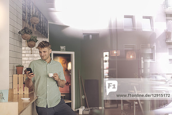 Young business owner drinking coffee  checking smartphone