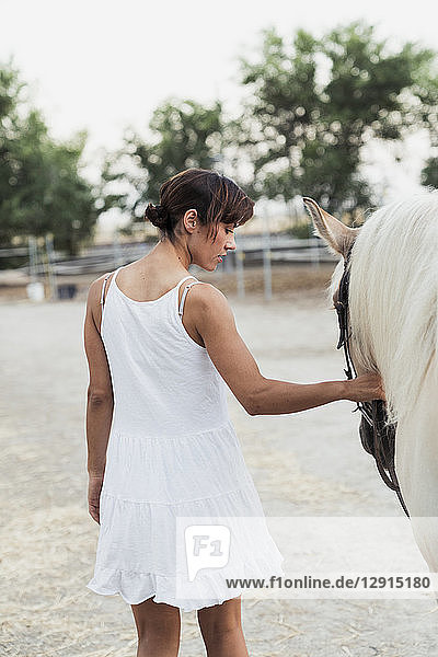 Back view of woman in white dress leading horse