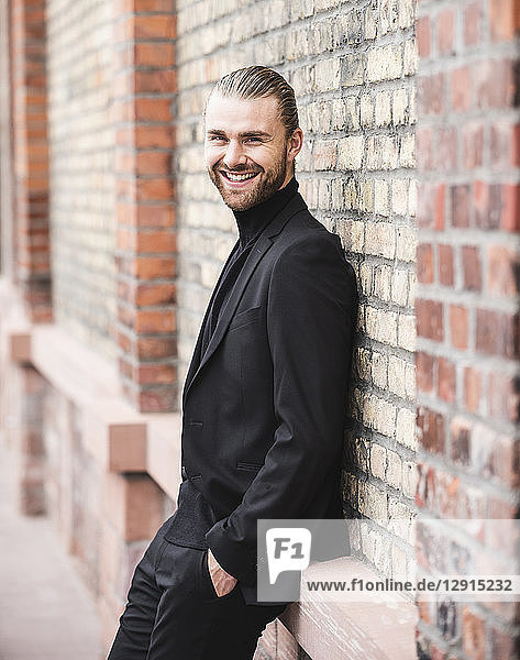 Portrait of smiling fashionable young man leaning against brick wall