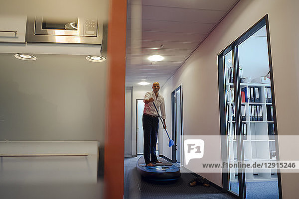 Businessman standing on paddle board  exercising in office corridor