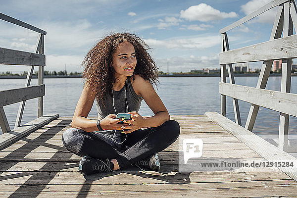 Young athletic woman sitting at the riverside using smartphone