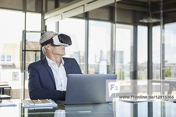 Businessman sitting at desk with laptop  using VR goggles