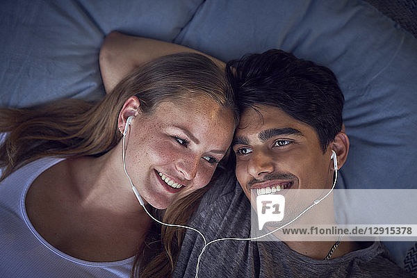 Young couple lying on cushions  sharing earphones  listening music