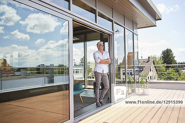Mature man relaxing standing at roof terrace at home