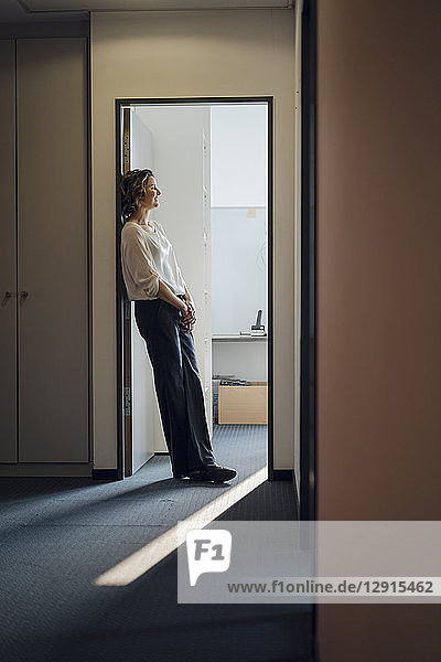 Businesswoman leaning relaxed in door frame of her office