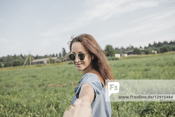 Smiling woman wearing sunglasses holding hand of partner in rural field