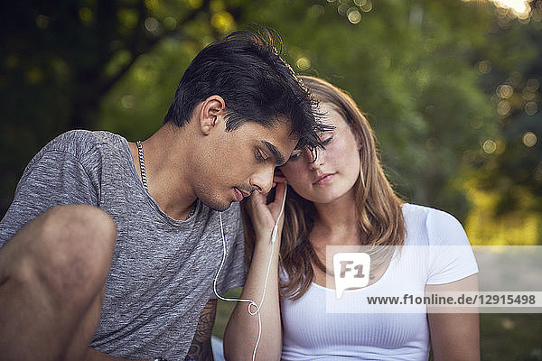 Young couple sitting in park  sharing earphones  listening music