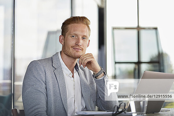 Portrait of confident businessman with laptop on desk in office