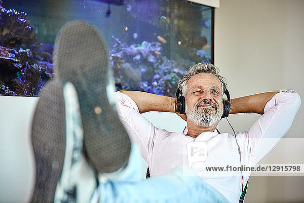 Relaxed mature man listening to music with headphones in front of aquarium