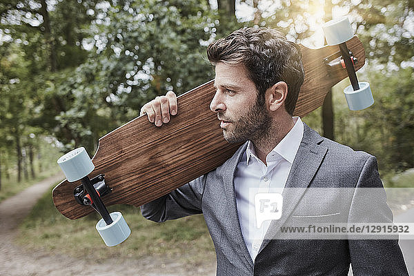 Portrait of businessman carrying skateboard on rural road
