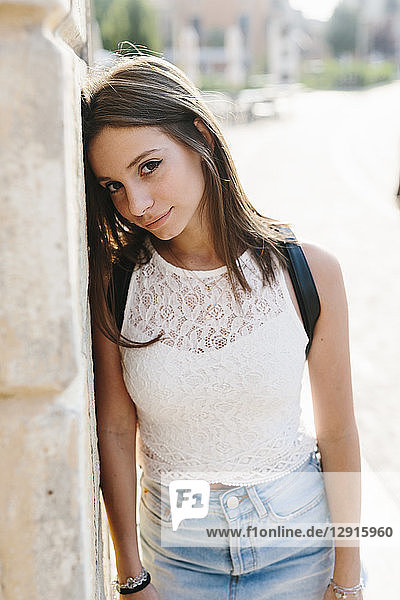 Portrait of smiling young woman leaning against a wall in the city