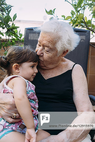 Grandmother kissing her granddaughter on terrace