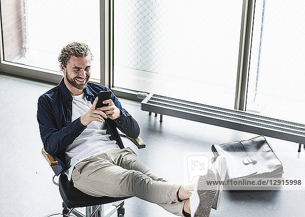 Smiling casual businessman sitting in office with feet up using cell phone