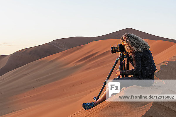 Africa  Namibia  Namib desert  Naukluft National Park  female photograper photographing at early morning light  sitting on sand dune