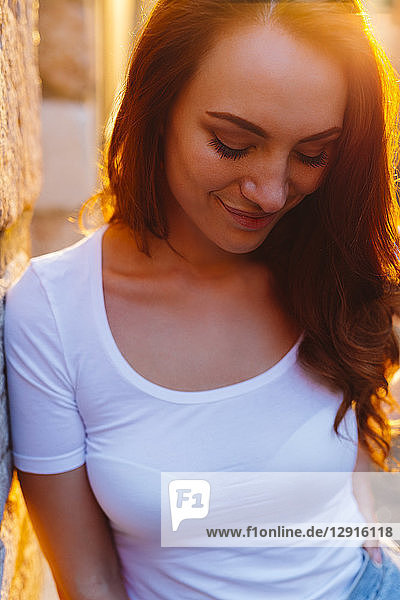 Portrait of smiling redheaded woman leaning against wall at sunset