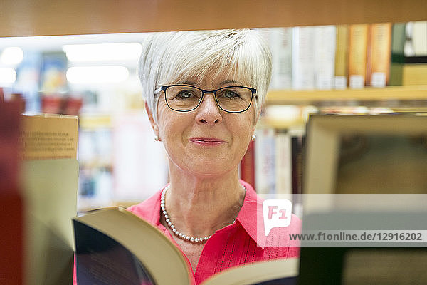 Portrait of smiling senior woman with book in a city library