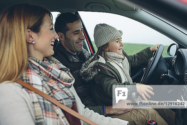 Happy family in car with little girl on father's lap pretending to drive