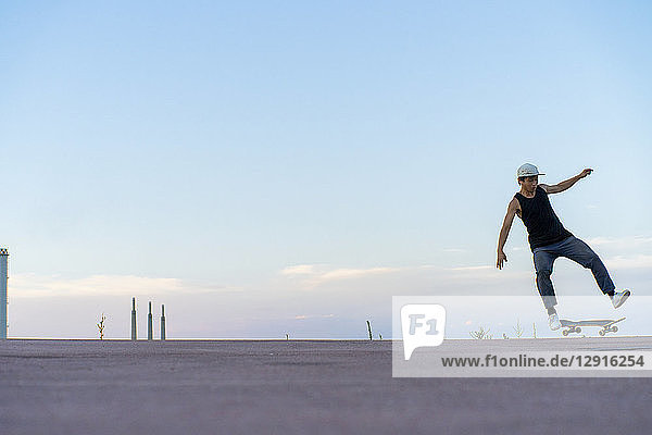 Young man doing a skateboard trick on a lane at dusk
