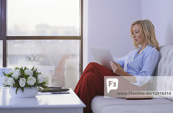 Blond woman sitting on couch  using laptop
