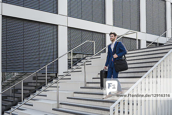 Smiling businessman with baggage in the city walking down stairs