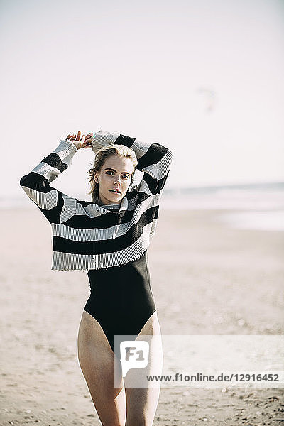 Portrait of a young woman standing on the beach wearing a pullover