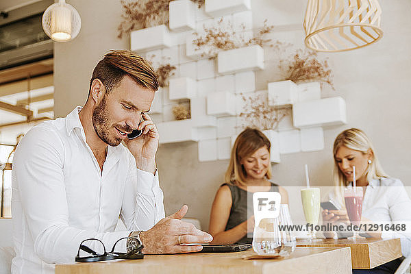 Man on cell phone in a cafe with two women in background