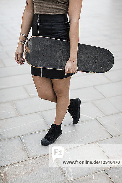 Low section of young woman carrying skateboard