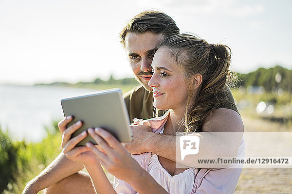 Smiling couple at the riverside in summer holding tablet