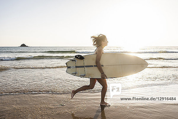 Young woman running on beach  carrying surfboard