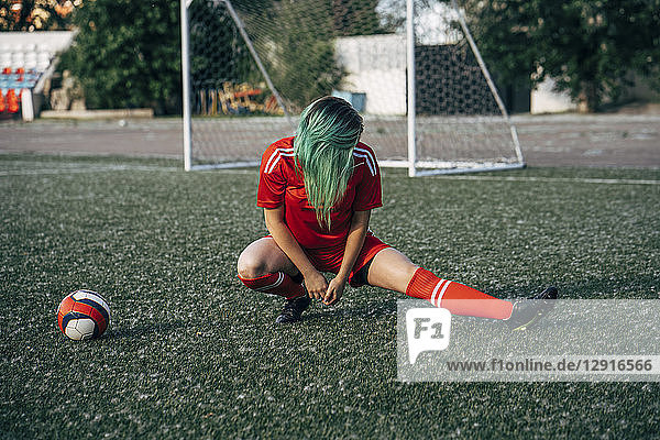 Young woman stretching on football ground next to the ball