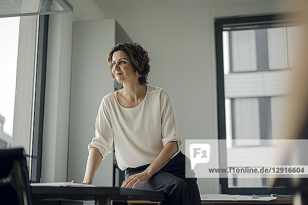 Successful businesswoman sitting on desk in her office