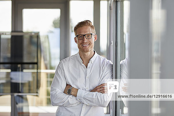 Portrait of smiling businessman in office leaning against window