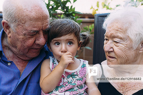 Grandparents looking at baby girl sucking thumb