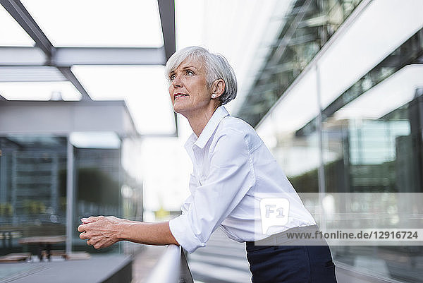 Senior woman leaning on railing in the city looking up