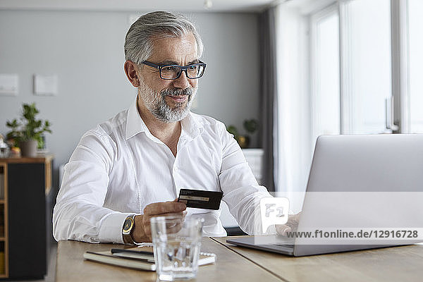 Portrait of content mature man paying online with credit card at home