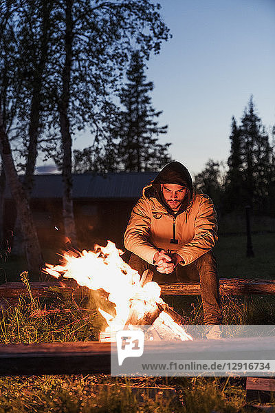 Young man sitting at a campfire  watching the flames