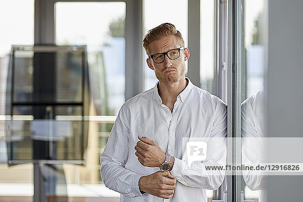Portrait of grimacing businessman in office leaning against window
