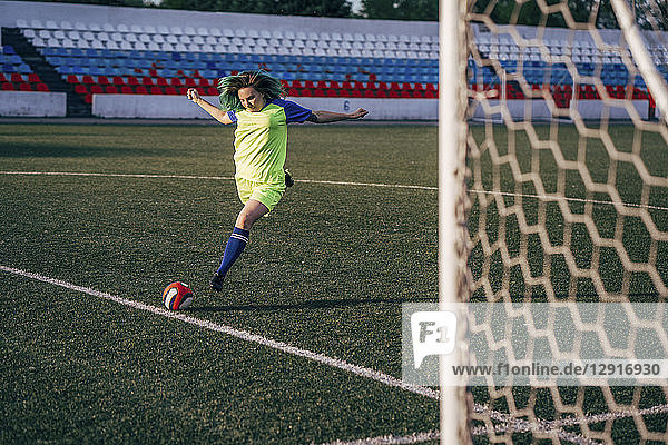 Young woman playing football on football ground shooting the ball