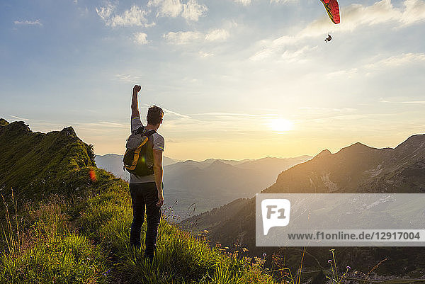 Germany  Bavaria  Oberstdorf  man on a hike in the mountains at sunset with paraglider in background
