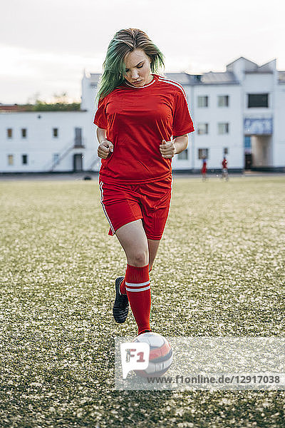 Young woman playing football on football ground running with the ball