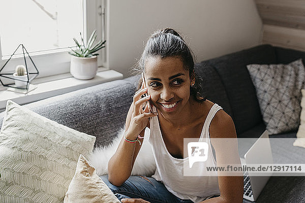 Portrait of smiling young woman on the phone sitting on the couch at home