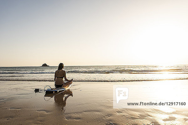 Young woman practicing yoga on the beach  sitting on surfboard  meditating