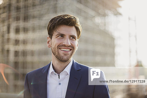 Portrait of smiling businessman in front of construction site looking sideways