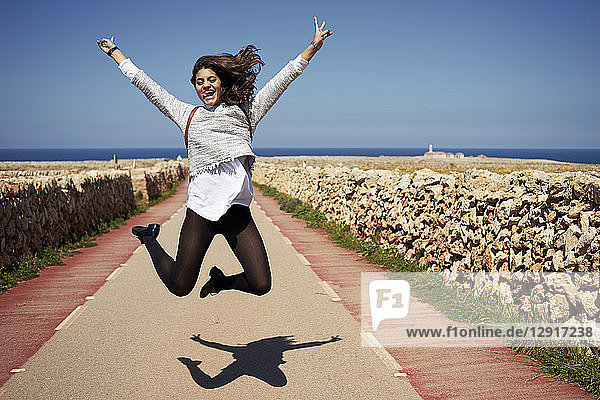 Cheerful young woman jumping in air with rising hands  outdoors