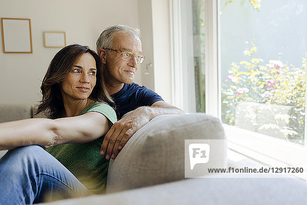 Smiling mature couple sitting on couch at home looking out of window
