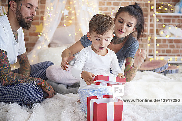 Surprised boy opening Christmas present with his parents in bed