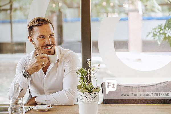 Smiling man with tablet drinking espresso in a cafe