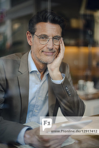 Mature businessman sitting in coffee shop  using digital tablet