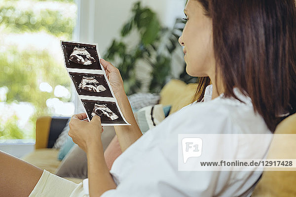 Woman looking at ultrasound pictures of unborn child on couch